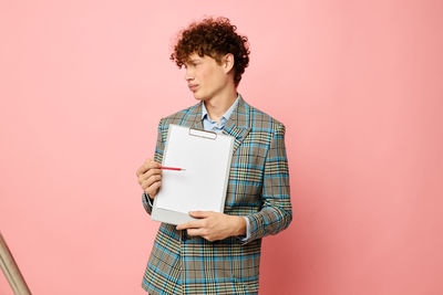 Young businessman holding clipboard against colored background