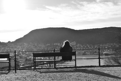 Rear view of woman sitting on mountain against sky