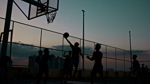 Silhouette people playing soccer against sky during sunset