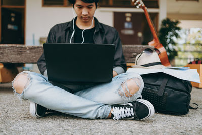 Low section of man using laptop while sitting outdoors