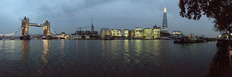 Illuminated city by sea against sky