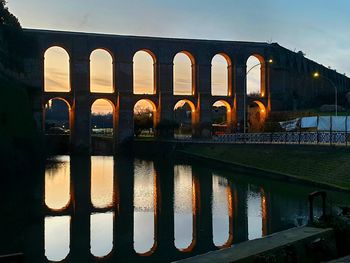 Arch bridge over river against sky during sunset
