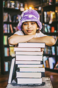 Portrait of young woman leaning on stack of books in bookstore
