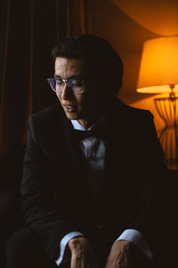 Dark portrait of young man in the classic suit and glasses looking away