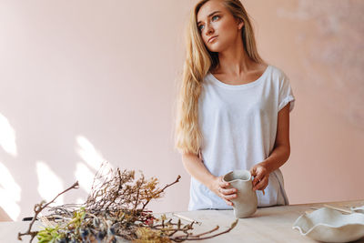 Beautiful young woman looking away while carving on pot over table