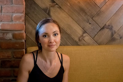 Portrait of smiling young woman standing against brick wall