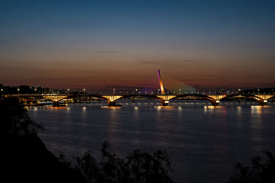 Illuminated bridge over river at sunset