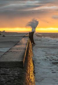 Waves splashing on groyne against sky during sunset