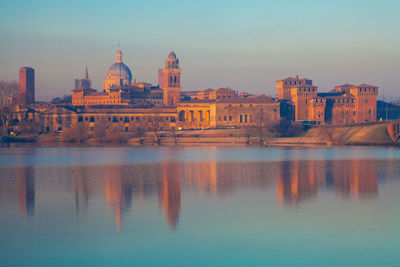 The skyline of city of mantova italy at sunrise reflected on waters of river mincio
