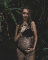 Portrait of smiling pregnant woman covered in dirt standing against plants