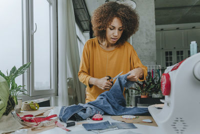 Fashion designer cutting jeans with scissors in workshop