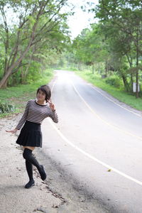 Portrait of young woman standing on road amidst trees in forest