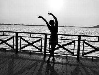 Woman with arms raised dancing by railing against sea