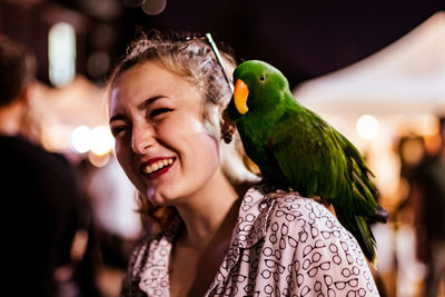 Close-up of happy woman with parrot on shoulder at night