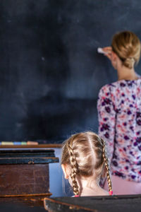 Rear view of teacher teaching female student in classroom