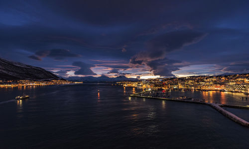 Illuminated city by sea against sky at night