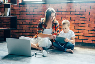 Working mother and son sitting on the floor use electronic devices for work and play.