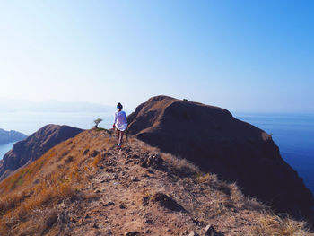 Rear view of woman hiking on mountain by sea against clear sky