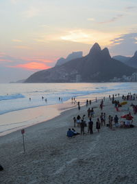 People enjoying vacation at beach with mountain in background during sunset