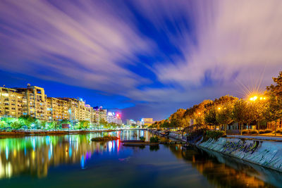 Illuminated city by river against sky at night