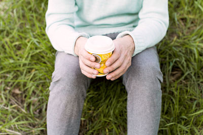 Midsection of person holding paper coffee cup while sitting on grass