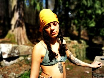 Young woman looking away while standing against tree