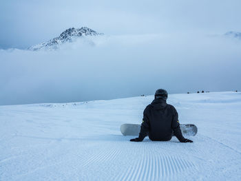 Person sitting on snow covered field against sky