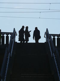 Low angle view of silhouette people standing on stairway against clear sky