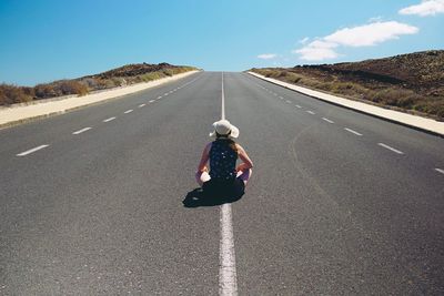 Rear view of woman sitting on country road during sunny day