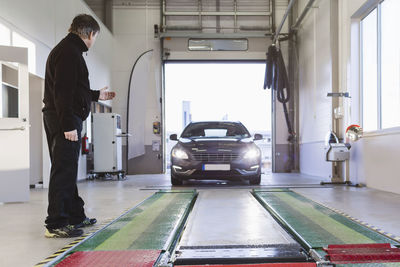 Full length of mechanic guiding car coming towards hydraulic lift