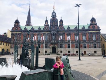 Portrait of cute girl sticking out tongue while standing by fountain against church