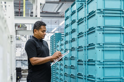 Warehouse worker using tablet pc amidst containers in industry