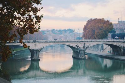 Arch bridge over river in city against sky