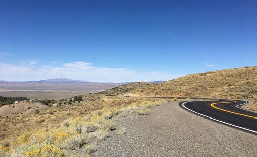 Scenic view of road by mountains against blue sky