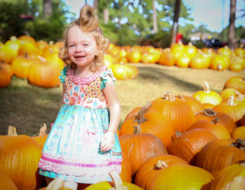 Portrait of happy girl standing amidst pumpkins at park during autumn