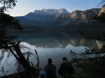 Two friends in the early morning by still lake in the rocky mountains