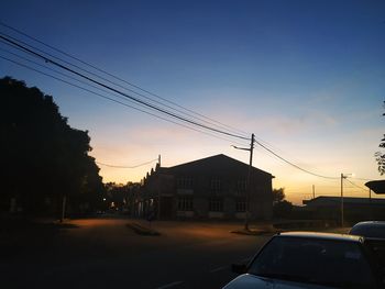 Cars on street by buildings against sky at sunset