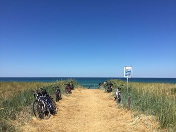 Bicycles parked on pathway amidst grassy field against clear blue sky