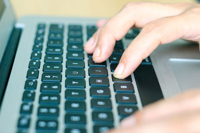 Cropped hands of person using laptop on wooden table