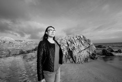 Young woman standing on rock by sea against sky