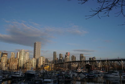 Boats in harbor by buildings against sky in city