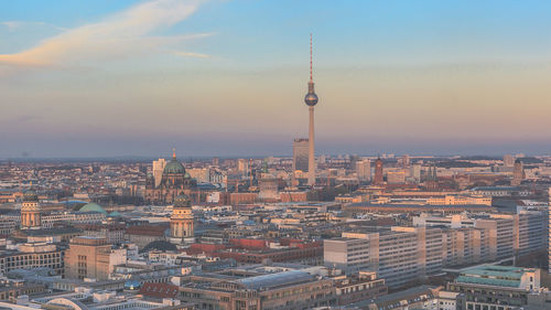 Fernsehturm amidst cityscape against sky during sunset