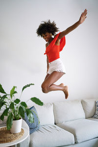 Happy black woman with curly hair having fun jumping dancing on the couch at home