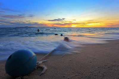 Buoy tied with rope at shore during sunset