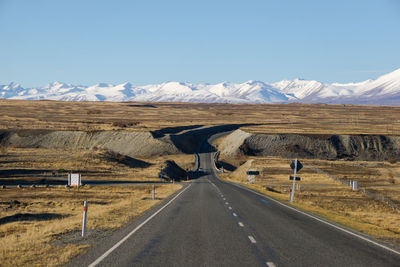 Road by snowcapped mountains against clear sky