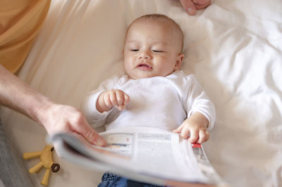 Father showing newspaper to baby on bed at home