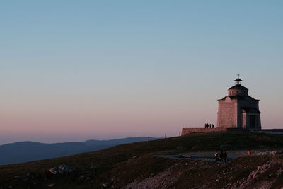Lighthouse by sea against clear sky during sunset