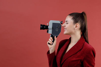 Young woman holding camera against yellow background