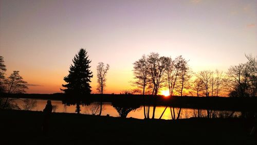 Silhouette trees by lake against sky during sunset