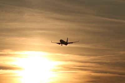Low angle view of silhouette airplane flying against sky during sunset